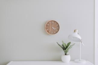 Image with a clock on the wall and a table with a plant and table lamp