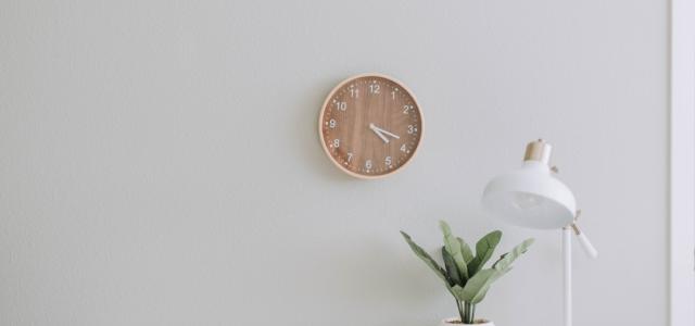 Image with a clock on the wall and a table with a plant and table lamp